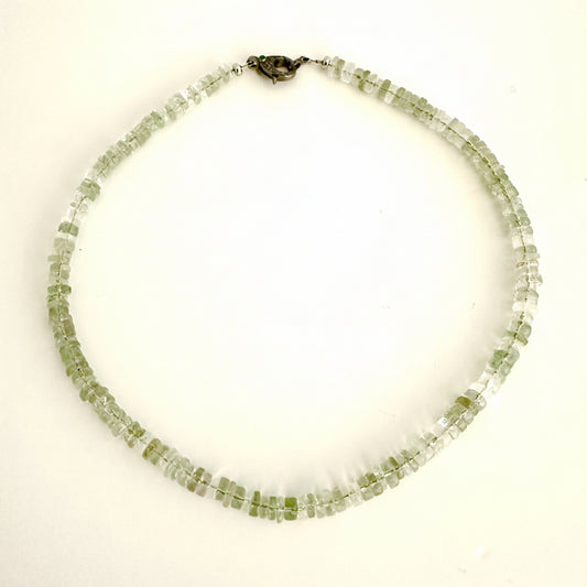A beaded necklace made of small, faceted light green gemstone beads, arranged in two rows and secured with a dark metal clasp, shown on a plain white background.
