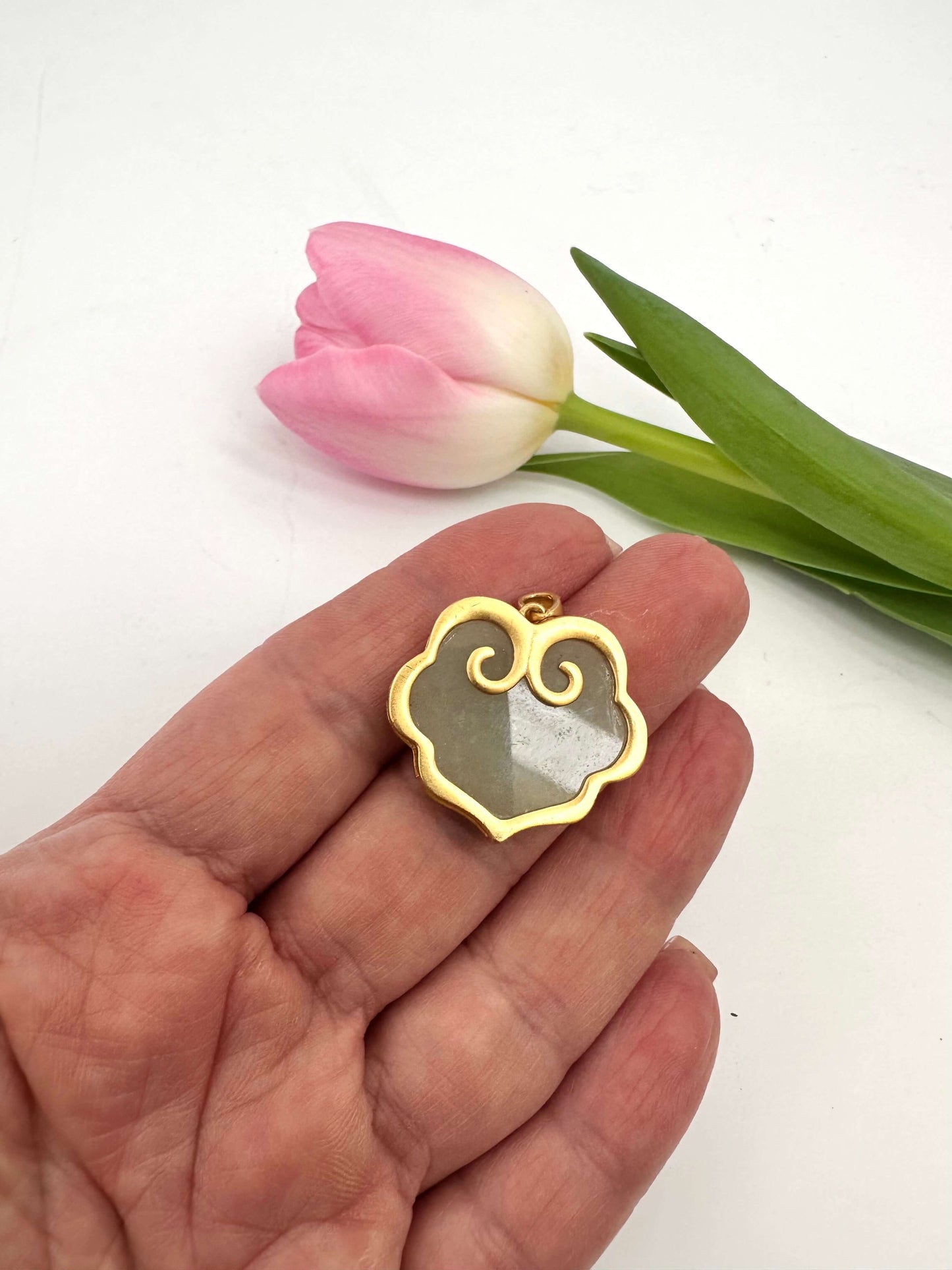 Hotan jade pendant in gold vermeil held in hand beside a pink tulip, showcasing natural nephrite charm.