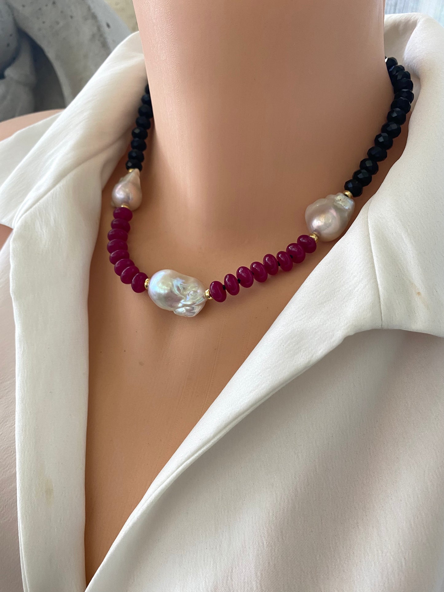 Necklace with pearls and red beads on a mannequin wearing a white shirt.