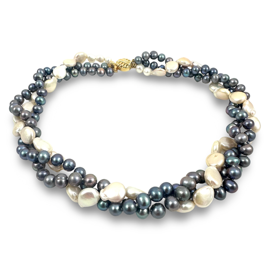 A multi-strand pearl necklace featuring dark gray and black baroque pearls alongside creamy white freshwater pearls, accented by a small gold clasp, shown on a plain white background.