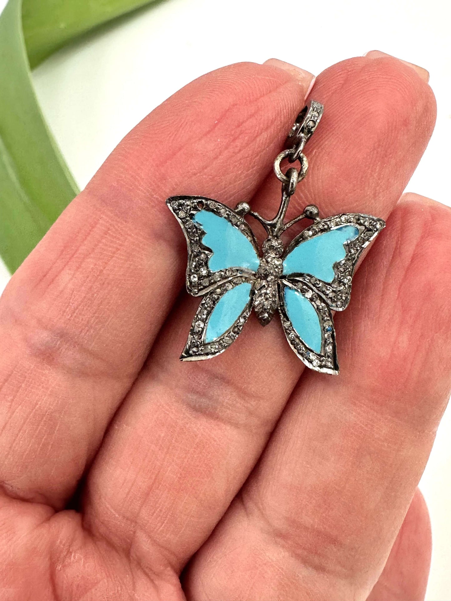 Blue enamel butterfly pendant with diamond pavé in sterling silver held in a hand.