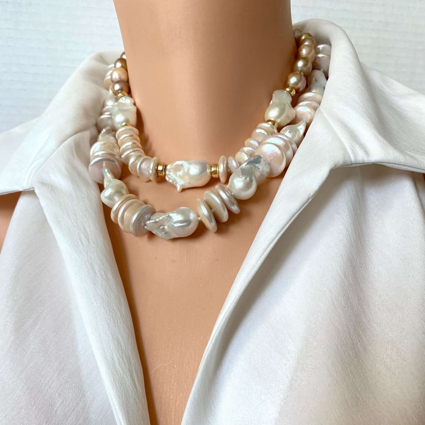 A close-up of a double-strand pearl necklace with baroque pearls and small gold spacer beads, worn on a mannequin torso wearing a white blouse.