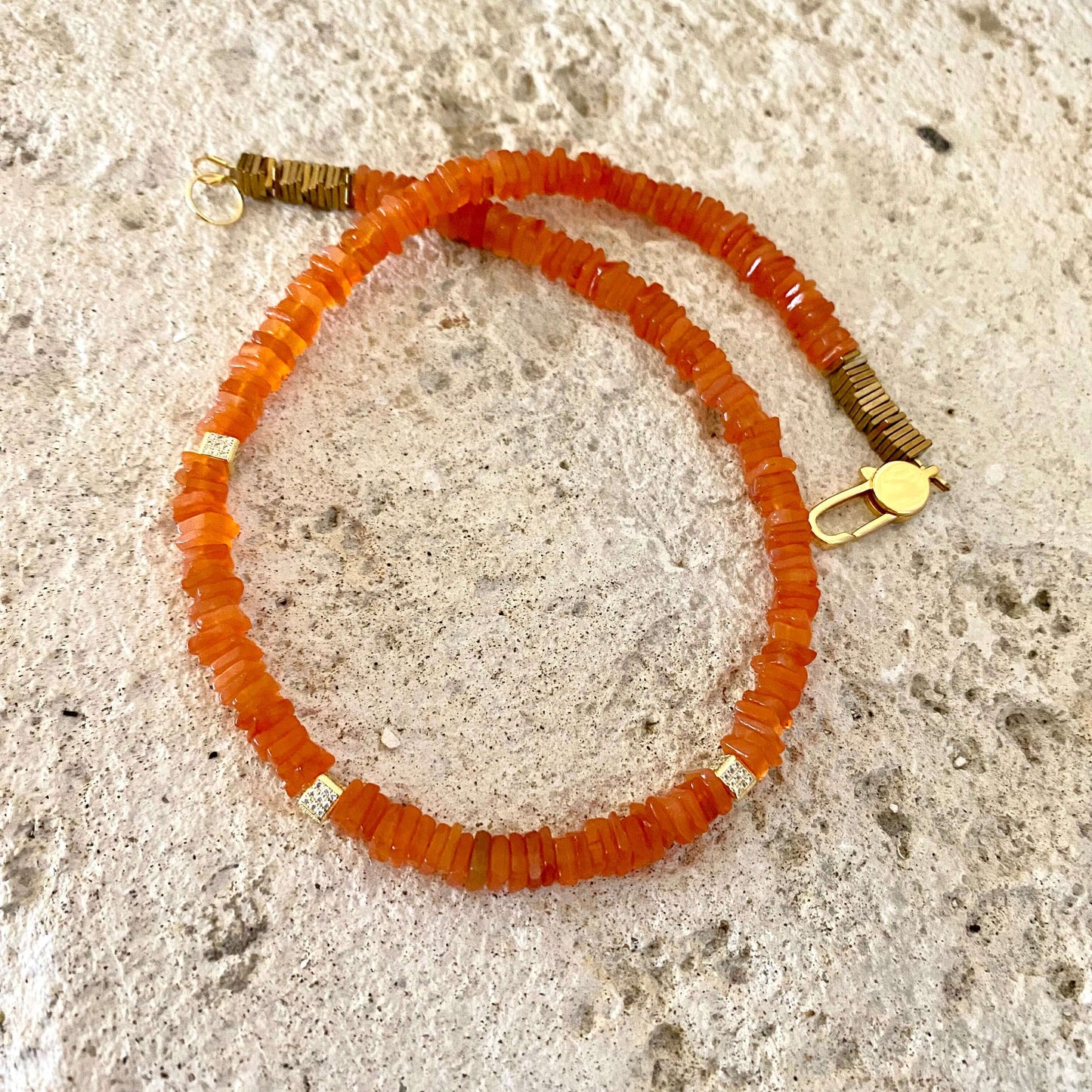 Carnelian choker necklace with bright orange gemstone beads displayed on textured background.