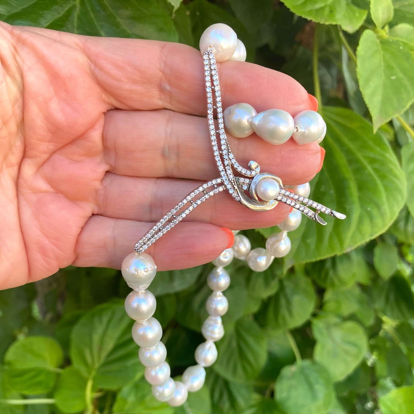 Natural white baroque pearl necklace with CZ pavé accent, close-up on leafy green backdrop.