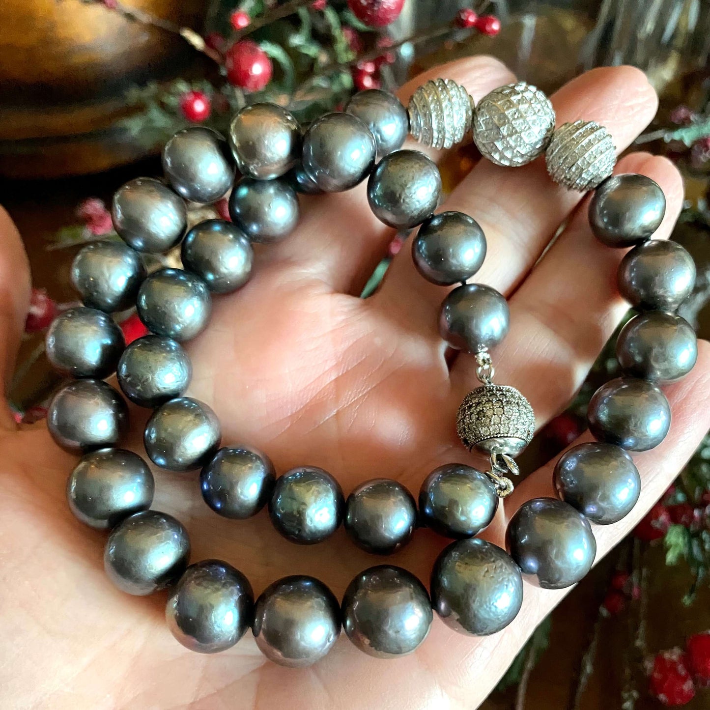 Close-up of black pearl silver necklace held in a woman’s hand against green leaf and mistletoe backdrop