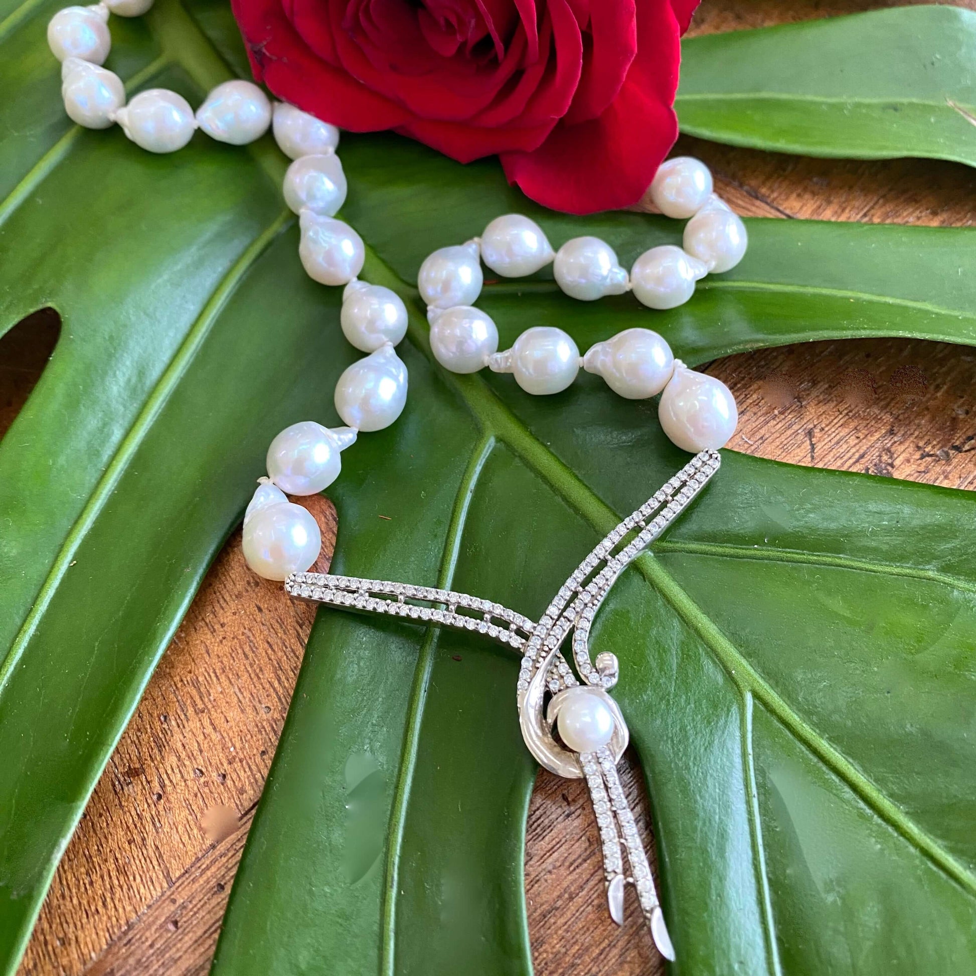 Handheld close-up of baroque pearl necklace on green leaf background, bridal jewelry detail.