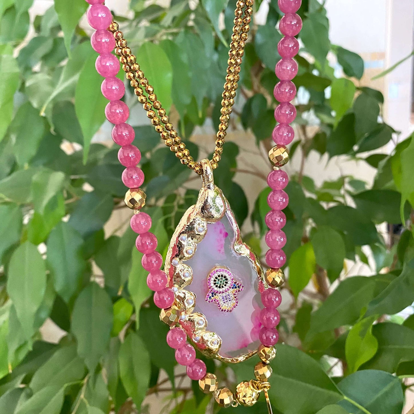 Hot pink agate pendant necklace showcasing a large gold-electroplated pendant with a CZ Hamsa symbol.