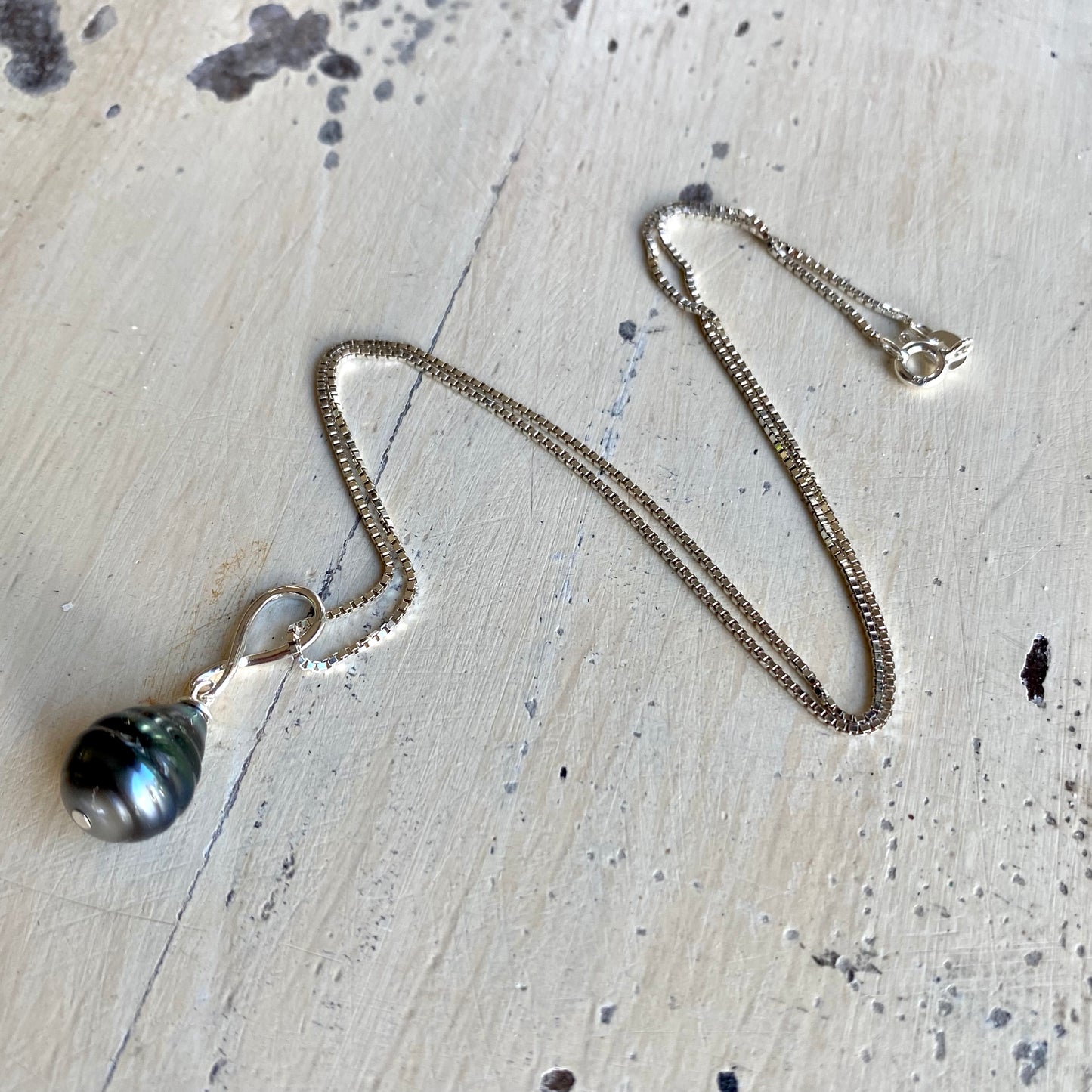 Tahitian teardrop pearl pendant box chain flat lay on tabletop, sterling silver box chain and pearl pendant